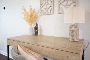 A wooden desk with a lamp, a vase with dried plants, and a decorative wall piece.