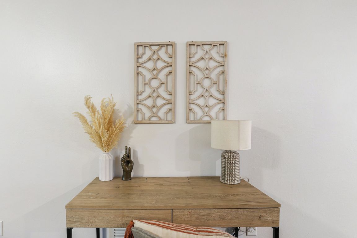 A wooden table with a lamp and decorative items, including a vase with dried plants and a wall-mounted panel.