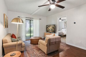 A living room with a sofa, armchair, ottoman, floor lamp, and a television. - 2BR Savannah condo w/ pool, WiFi, parking, full kitchen * 30+ days (Savannah)