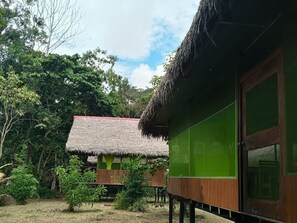 A traditional thatched-roof structure with a green exterior wall and a wooden deck.