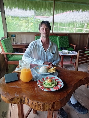 A man seated at a wooden table with a plate of food, a glass of orange juice, and a laptop.