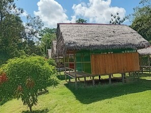 Une construction à toit de chaume dotée d’une terrasse en bois, entourée de verdure.