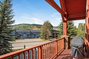 A wooden balcony with a grill, overlooking a parking lot and buildings with a mountainous backdrop. - Spacious Avon Townhome - Views of Beaver Creek (Avon)