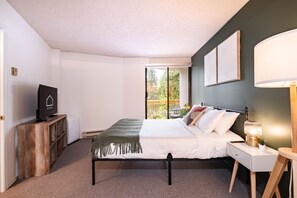 A bedroom with a bed, bedside table, lamp, and a television on a stand. - Mountain views | Ski-in/out | Pool, hot tub & gym (Whistler)