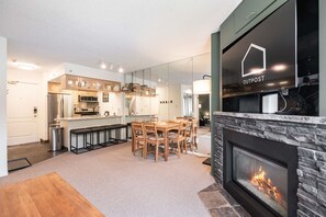A modern kitchen with a dining area, a fireplace, and a visible logo on the wall. - Mountain views | Ski-in/out | Pool, hot tub & gym (Whistler)