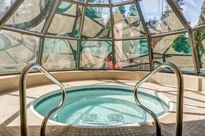 A hot tub with metal railings, surrounded by a tiled floor, and a glass enclosure with a view of trees and a road. - Mountain views | Ski-in/out | Pool, hot tub & gym (Whistler)
