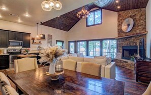 A spacious living area with a high ceiling, a stone fireplace, and large windows.