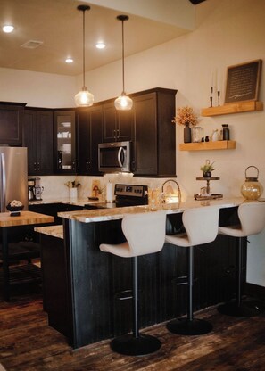 A modern kitchen with dark cabinets, a central island with bar stools, and pendant lighting.