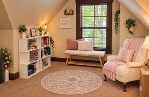A cozy reading nook with a bench, a bookshelf, and a window with a view of greenery.