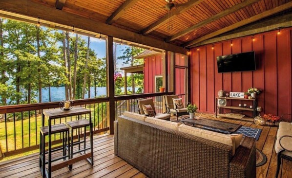 A covered outdoor seating area with a view of a lake, furnished with a sofa, chairs, and a table.