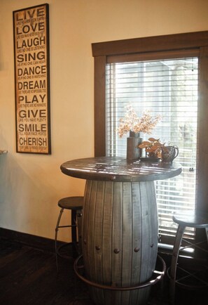 A round wooden table with a metal stool, a vase with flowers, and a wall with motivational quotes.