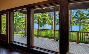 Una habitación con ventanas amplias que dan a una terraza con vistas a un lago y árboles.