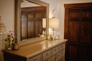 A wooden dresser with a mirror above it, a lamp, and a vase with flowers.