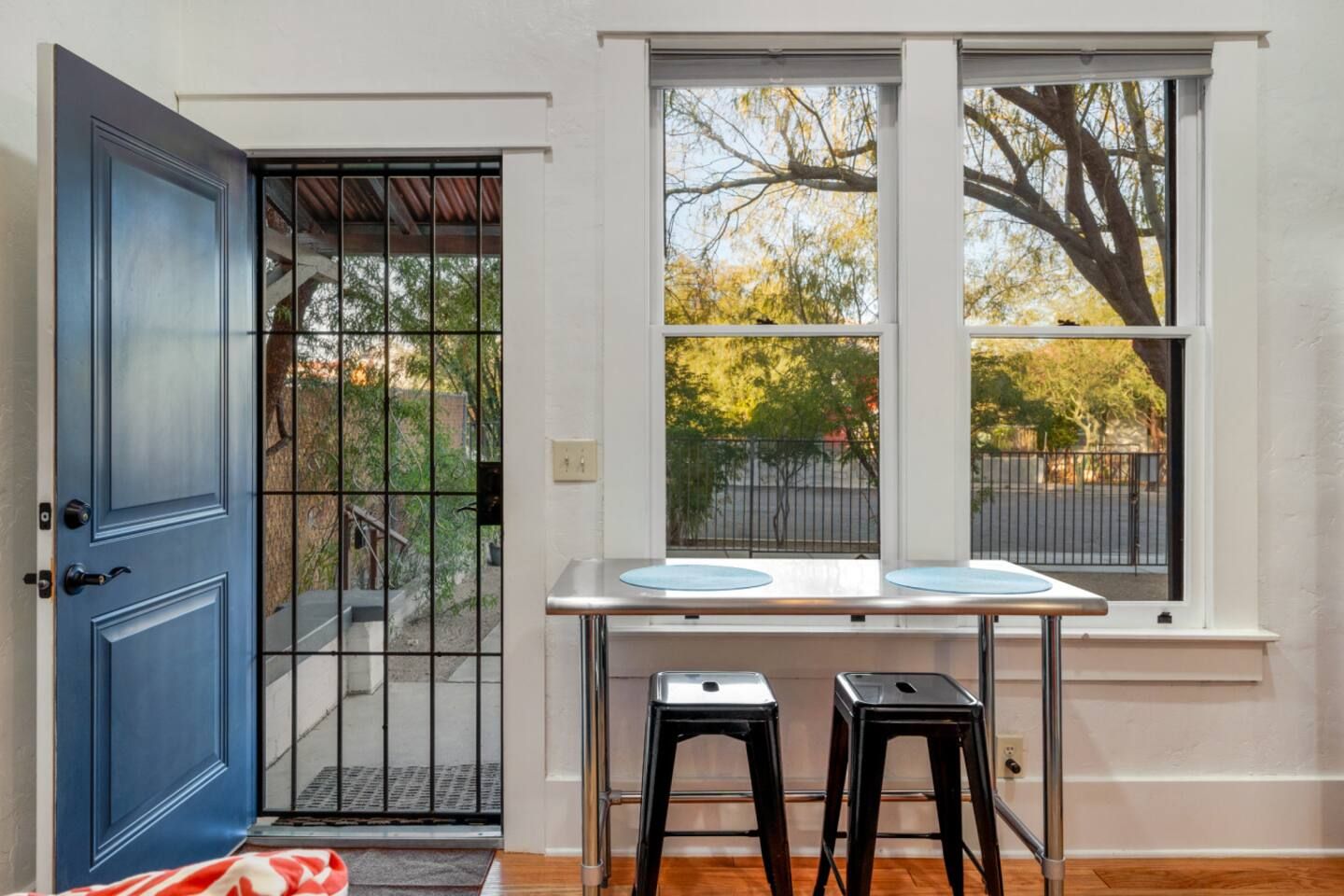 A room with a blue door, a window with a view of trees, and two stools.