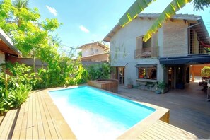 Ein Poolbereich mit Holzterrasse, umgeben von üppiger Vegetation und einem zweistöckigen Gebäude mit Balkon.