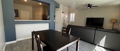 A dining area with a table and chairs, a kitchen with a counter, and a living area with a sofa and television.