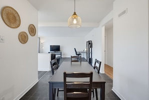 A modern dining area with a long table, chairs, a television, and a hanging light fixture.