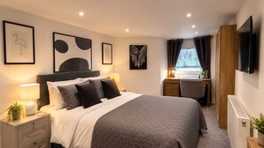 Une chambre à coucher avec un lit, une table de chevet, une lampe et des œuvres d’art accrochées aux murs.
