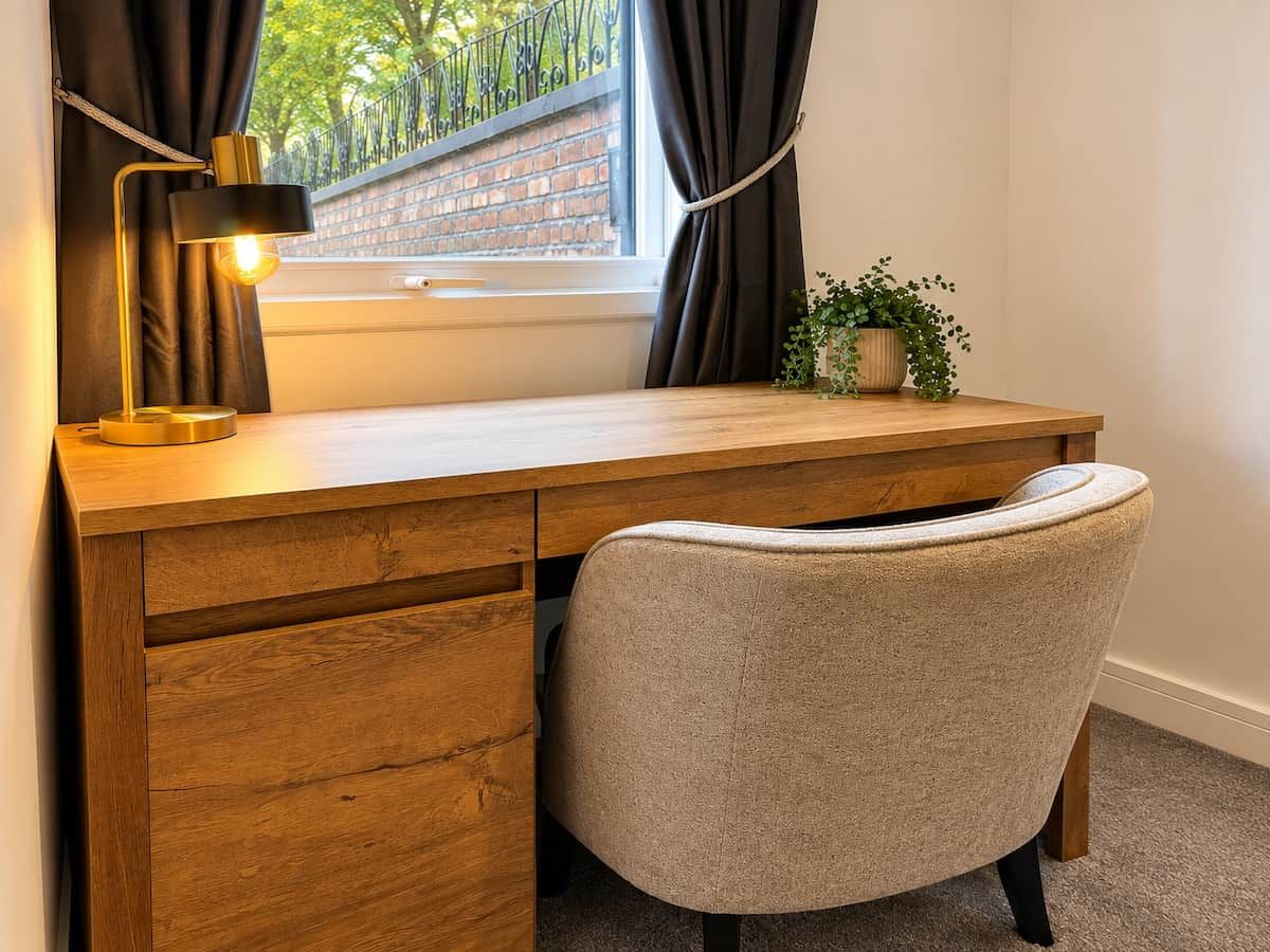 Een houten bureau met een lamp, een stoel en een potplant in een kamer met een raam.