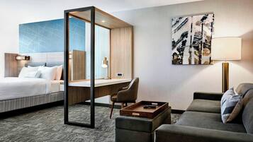 Una habitación de hotel con cama, escritorio, silla, sofá y un cuadro en la pared.