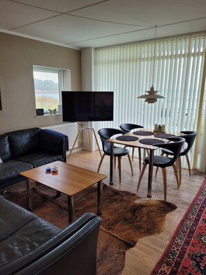 A living room with a sofa, a coffee table, a TV, a dining table with chairs, and a patterned rug. - Holiday apartment with a view (Hejlsminde)