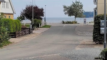 En asfalteret vej der fører til en strand, med boliger på den ene side og en bygning med et postkasse på den anden.