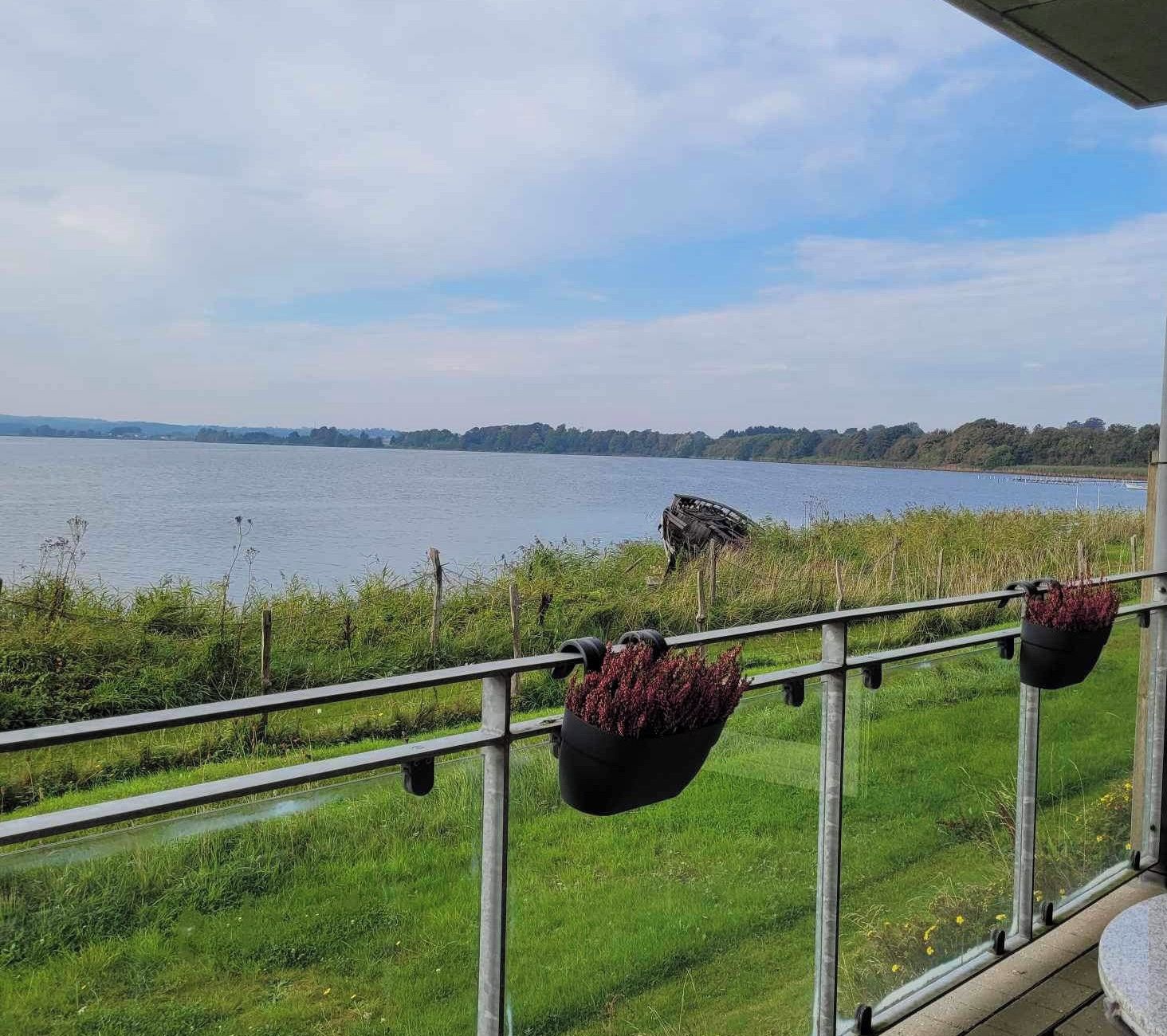 A balcony with a view of a lake, a railing, and hanging flower pots.