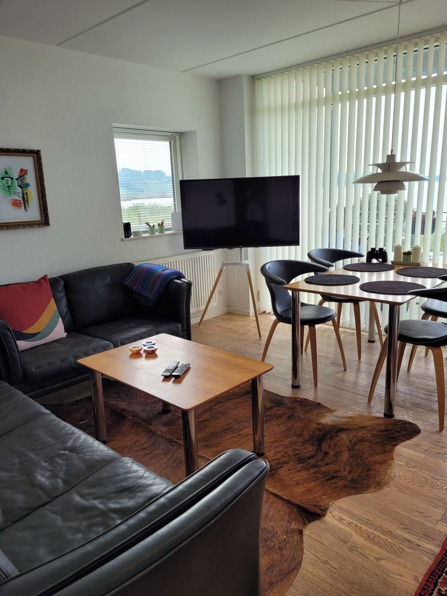 A living room with a black leather sofa, a wooden coffee table, a flat-screen TV, and a dining area with chairs and a table.