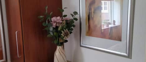Et værelse med et træskab, en stol, en vase med blomster og et indrammet abstrakt billede på væggen.