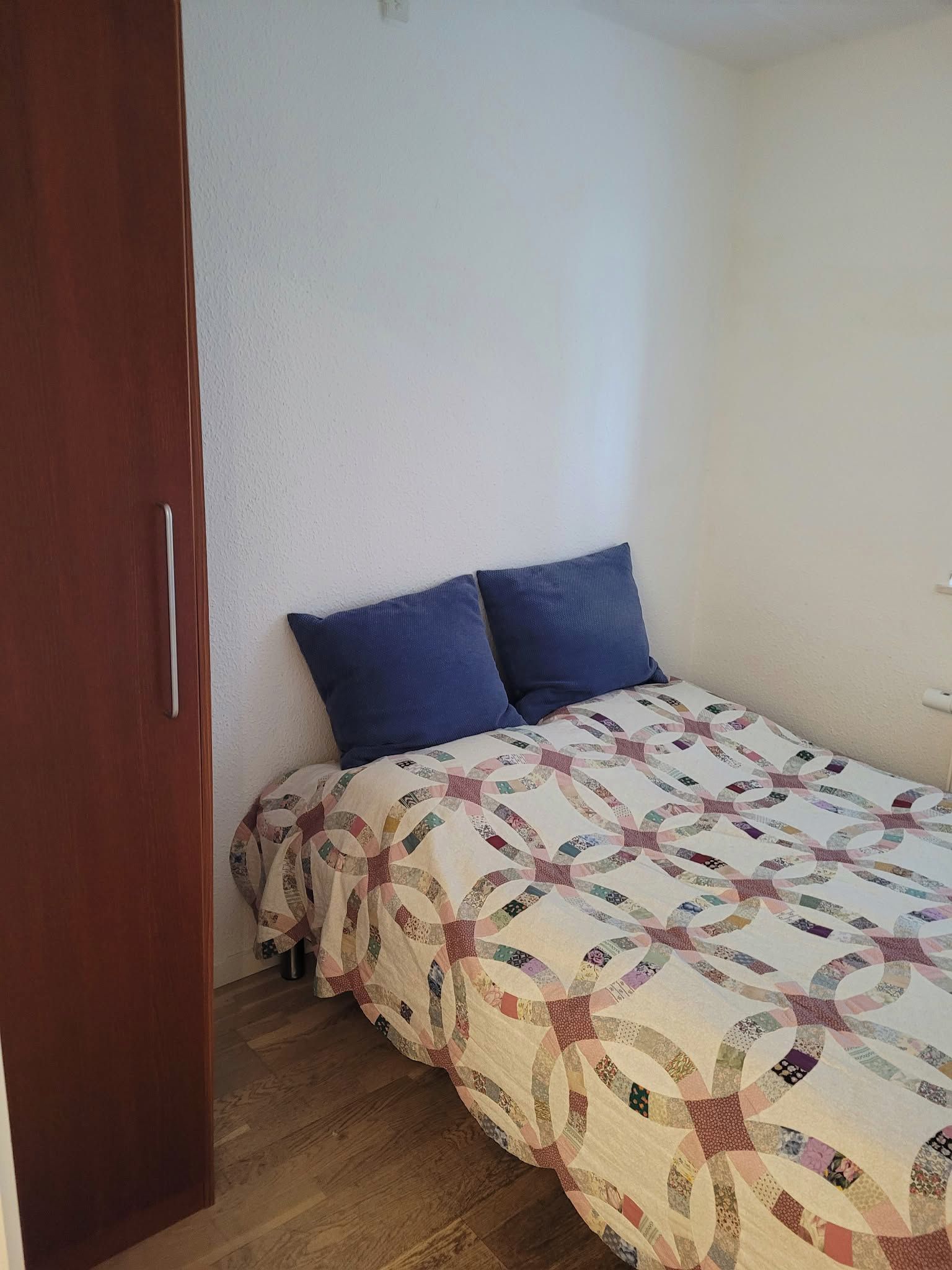 Een slaapkamer met een bed, twee kussens, een houten deur en een witte muur.