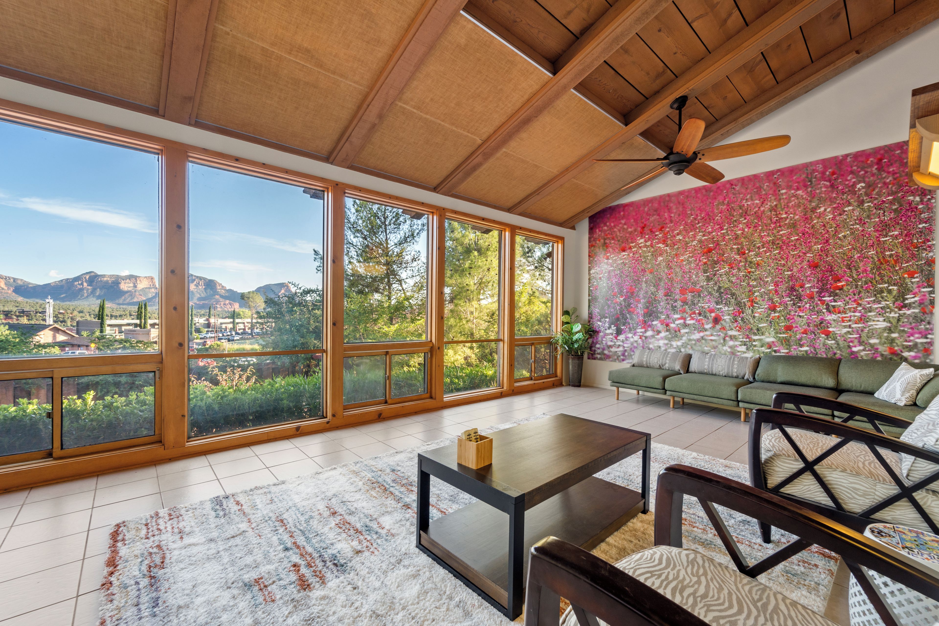 A spacious living area with large windows, a ceiling fan, and a vibrant flower wall.