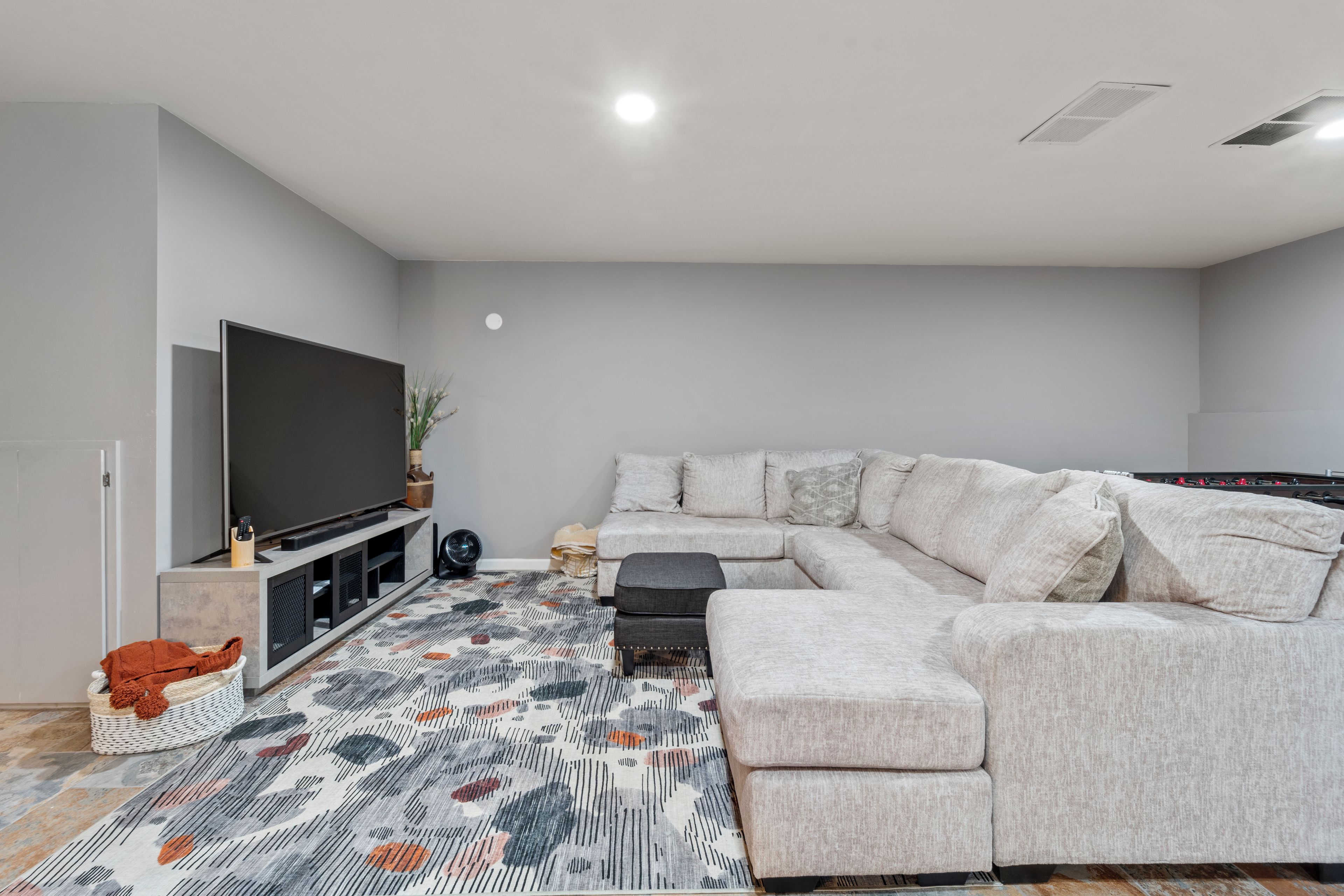 A modern living room with a sectional sofa, a flat-screen TV, and a patterned rug.