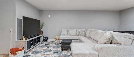 A modern living room with a sectional sofa, a flat-screen TV, and a patterned rug.