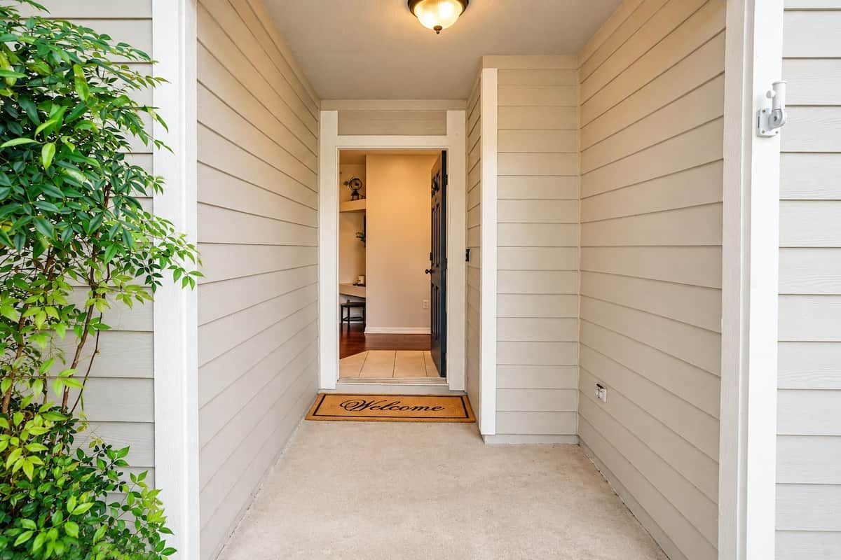 A narrow hallway with a welcome mat, a door leading to a room, and a plant on the left.