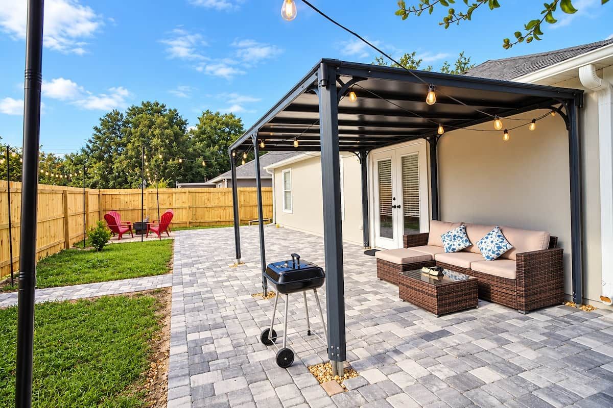 A covered patio area with a grill, outdoor seating, and string lights.