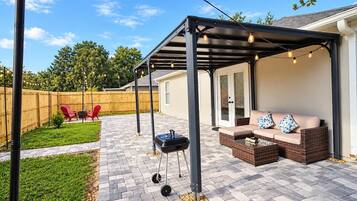 A covered patio area with a grill, outdoor seating, and string lights.