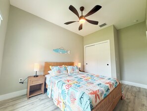 Ein Schlafzimmer mit einem Bett, Nachttisch, Deckenventilator und einer Wanddekoration mit Fischmotiven.