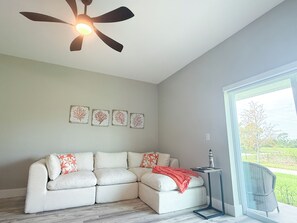 A room with a sectional sofa, a ceiling fan, wall art, and a view through a glass door. - 20 Min to Englewood Beach • Park + BBQ (Port Charlotte)