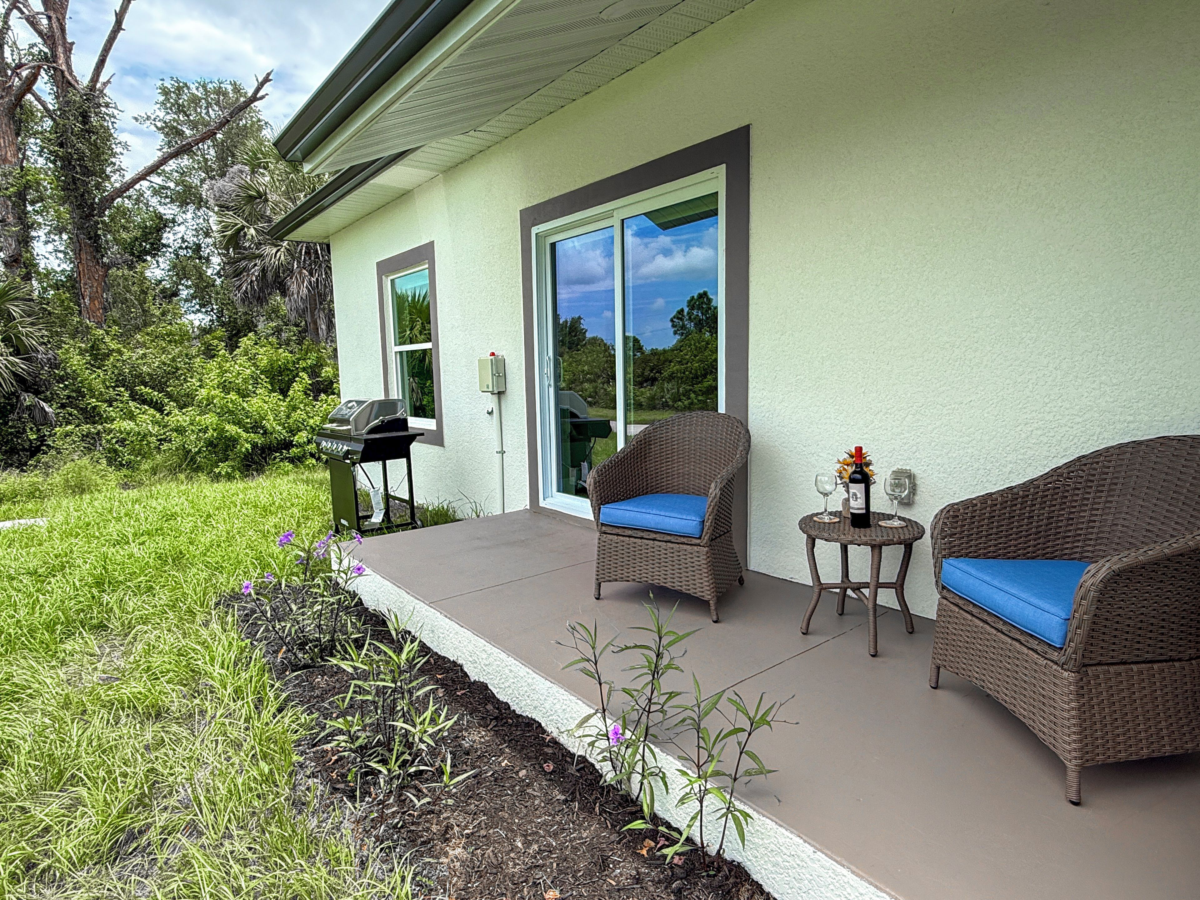 A patio with wicker furniture, a grill, and a table with a bottle and glasses.