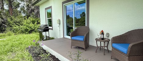 A patio with wicker furniture, a grill, and a table with a bottle and glasses.