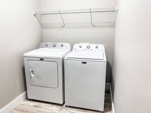 Ein Waschraum mit einer Waschmaschine und einem Trockner mit Frontlader, einem Metalltrockner darüber und einem Holzboden.