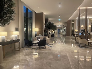 En rummelig hotellobby med skinnende marmorgulv, siddeområder og store vinduer.