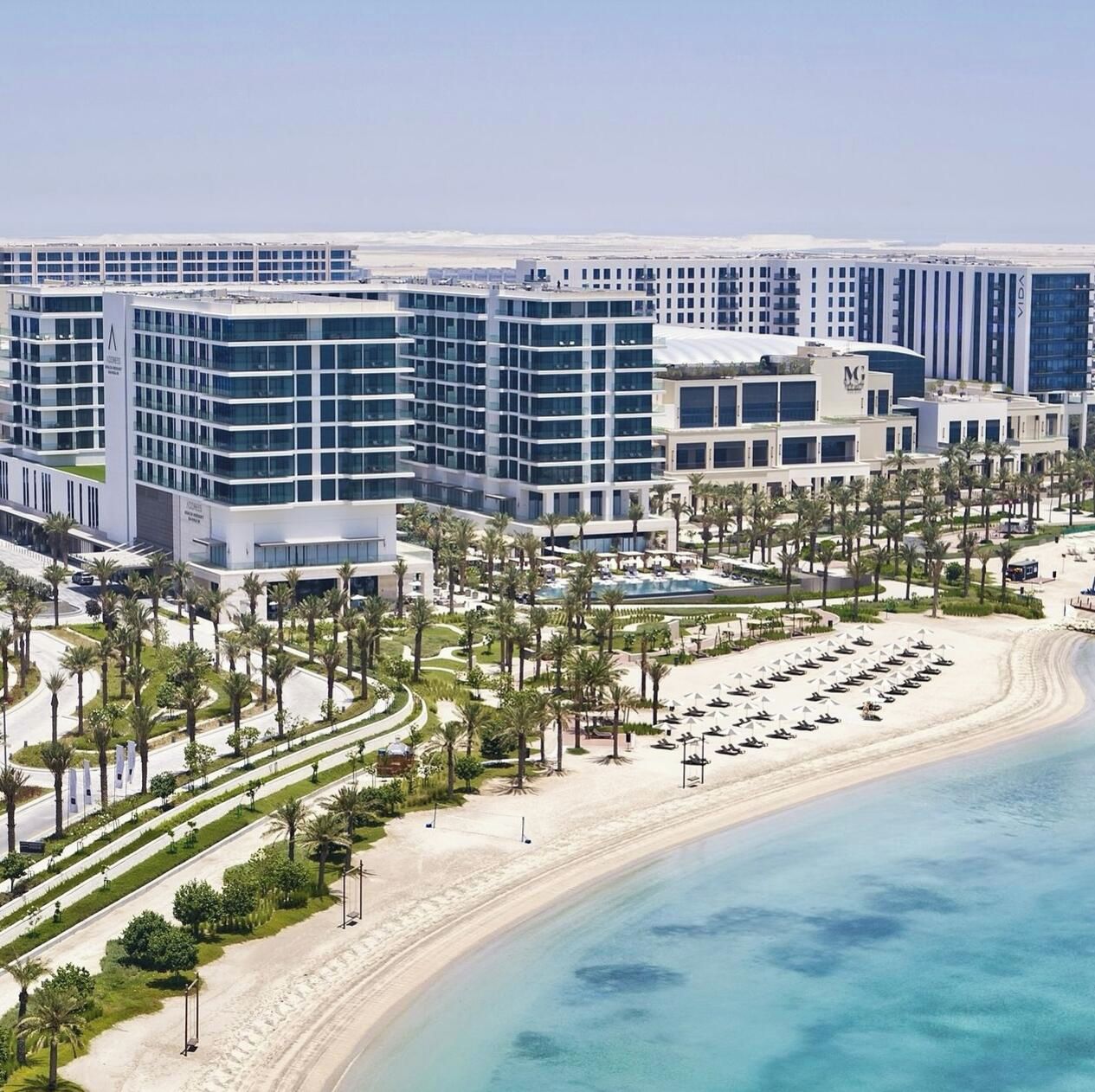 A modern hotel complex with multiple buildings, a beachfront, and a well-maintained garden area.