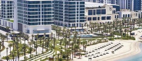 A modern hotel complex with multiple buildings, a beachfront, and a well-maintained garden area.