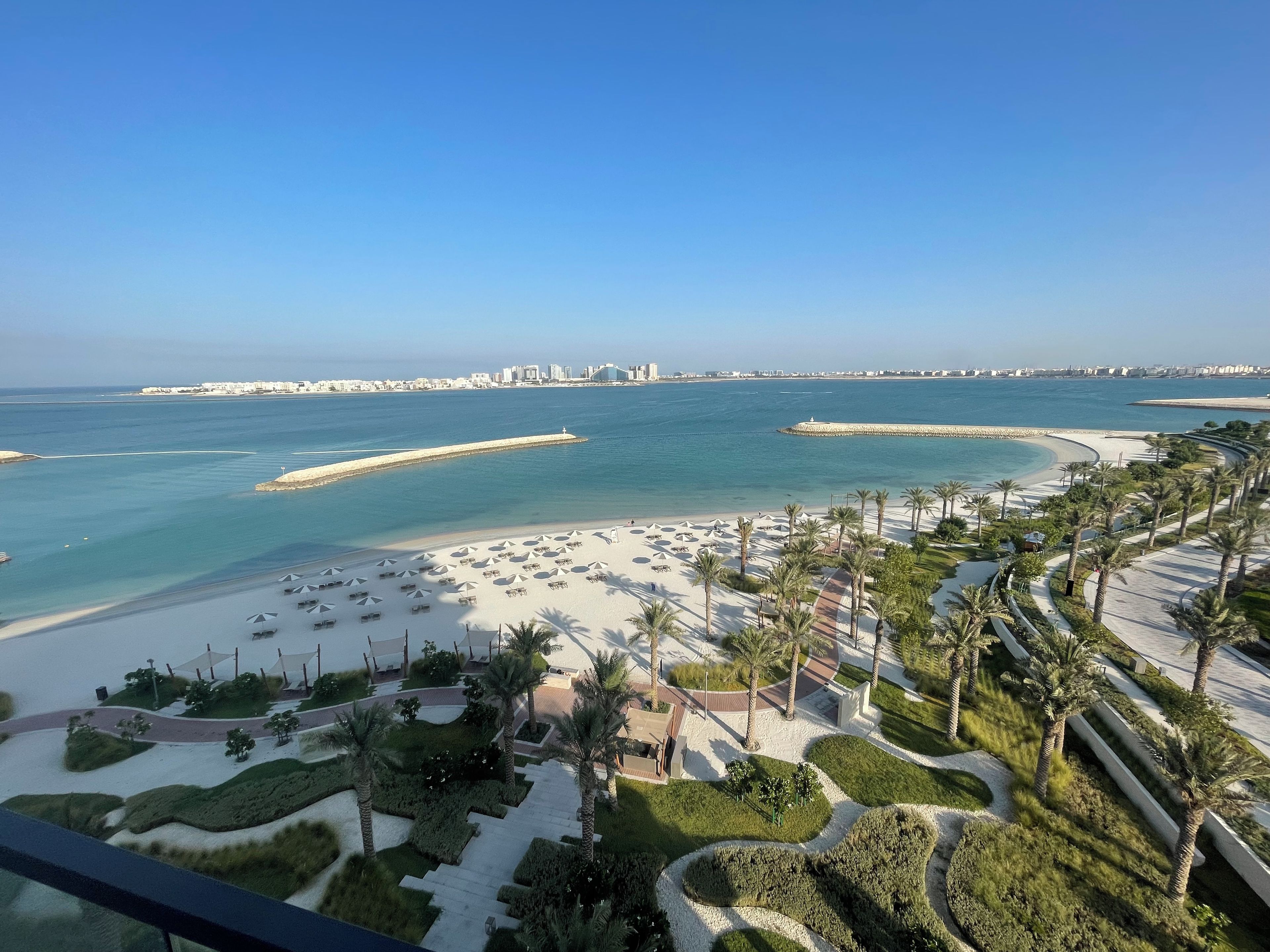 A coastal resort with a beach, palm trees, and a view of the city skyline.