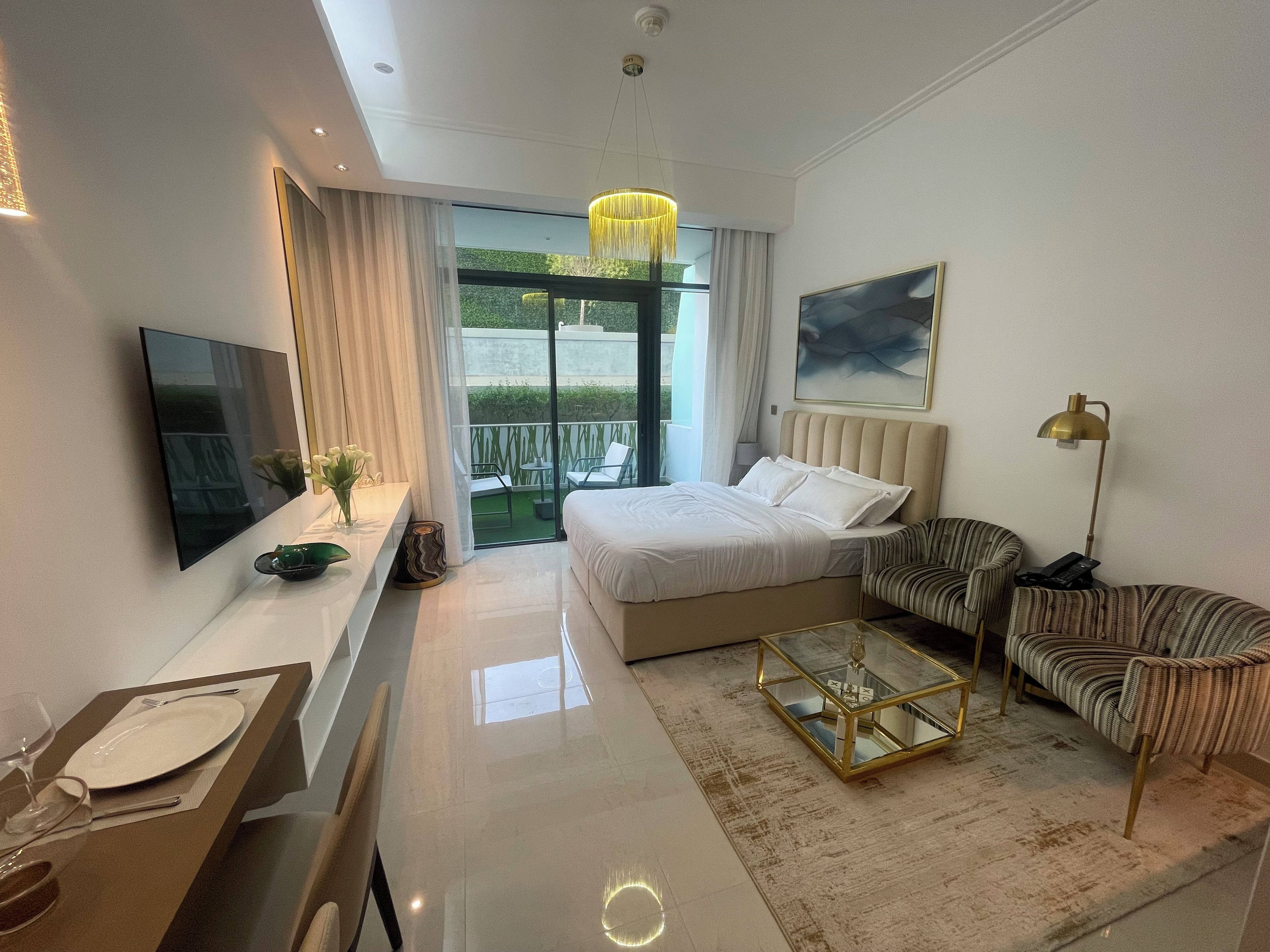 Ett modernt hotellrum med en säng, en soffa, en TV, ett skrivbord med en stol och en balkong med utemöbler.