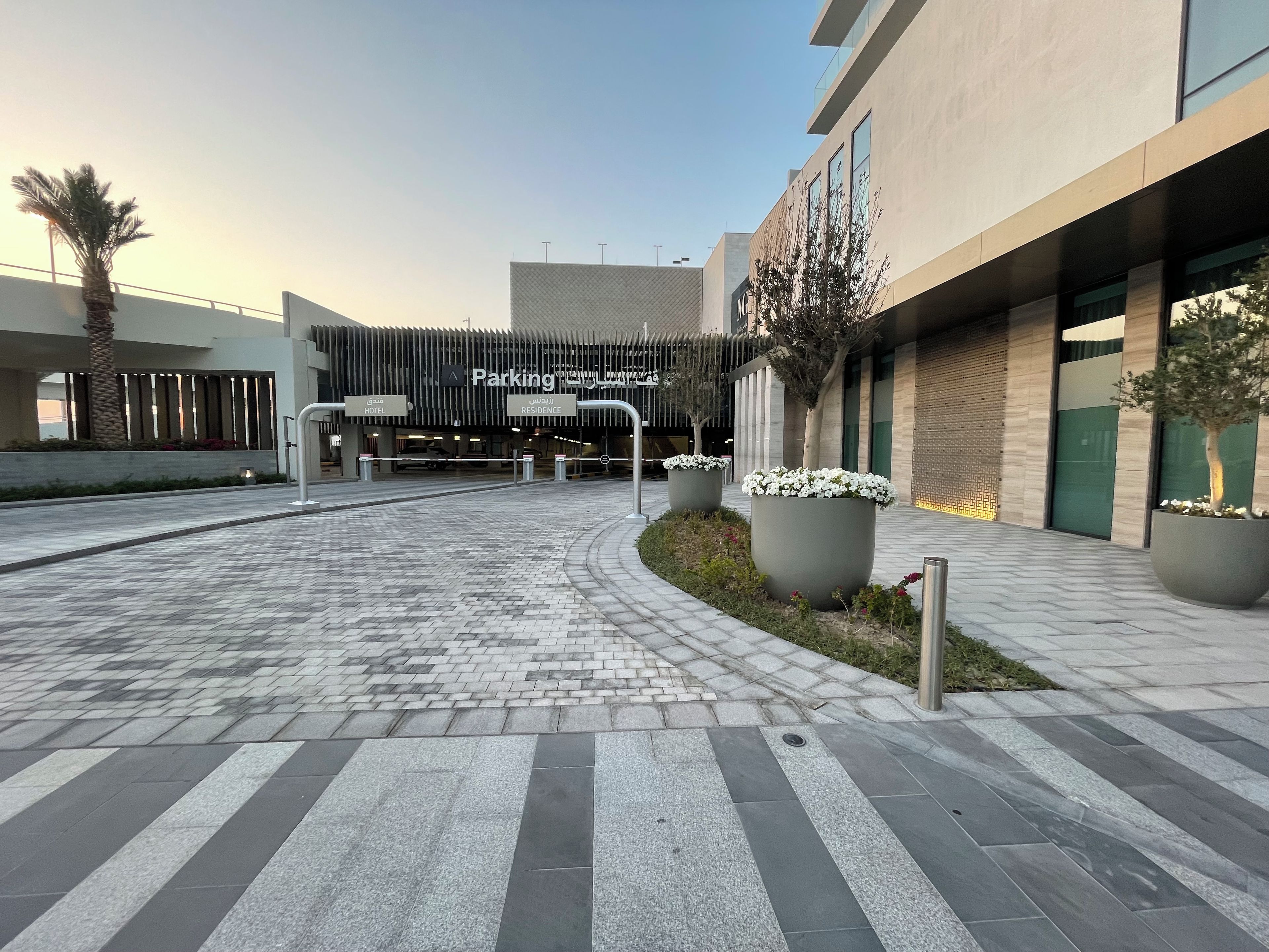 A modern building with a parking entrance, large planters with flowers, and a clear sky.