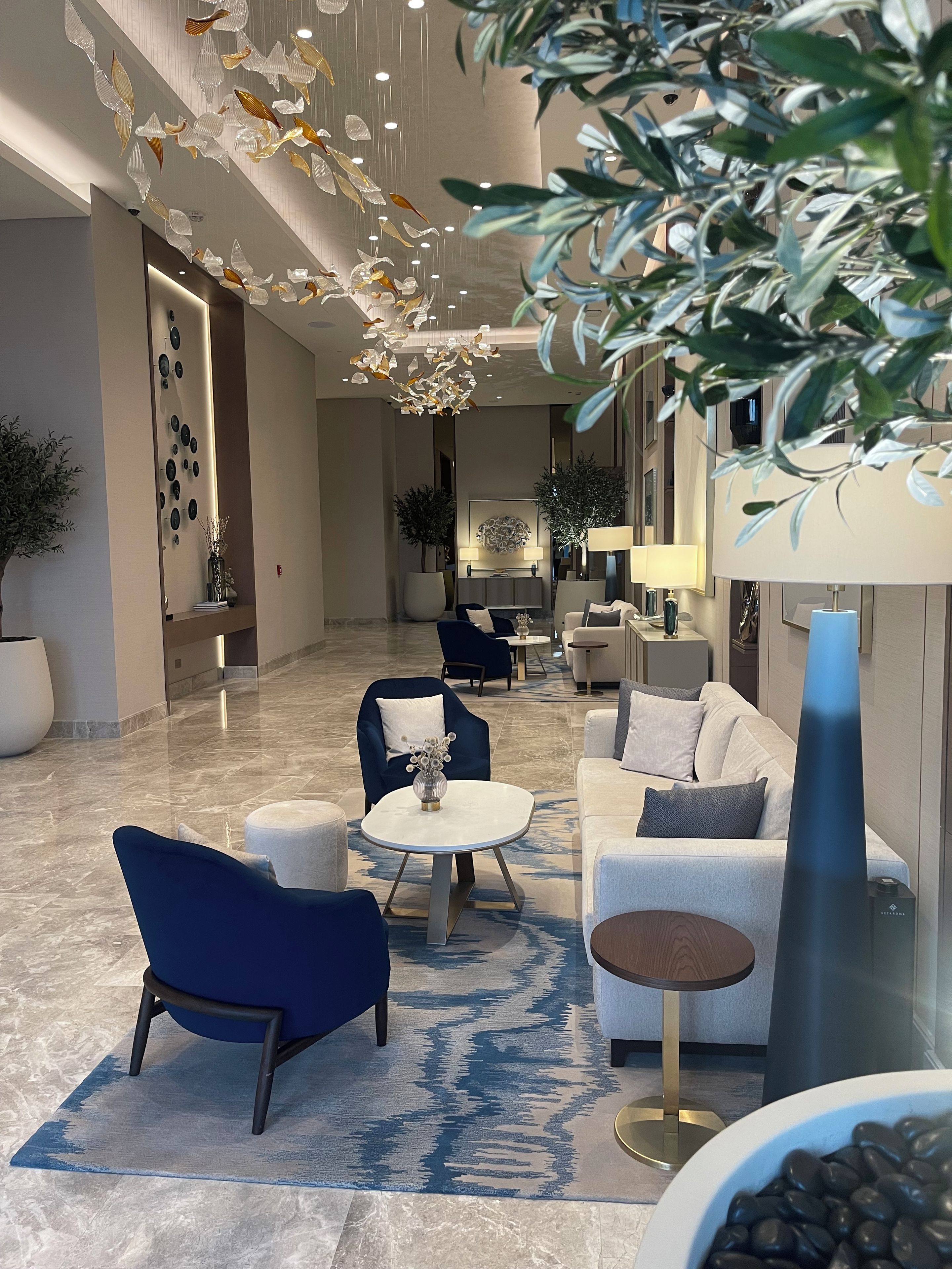Un intérieur moderne avec un coin salon comprenant un fauteuil bleu, une table ronde blanche et un canapé agrémenté d’un tapis à motifs.
