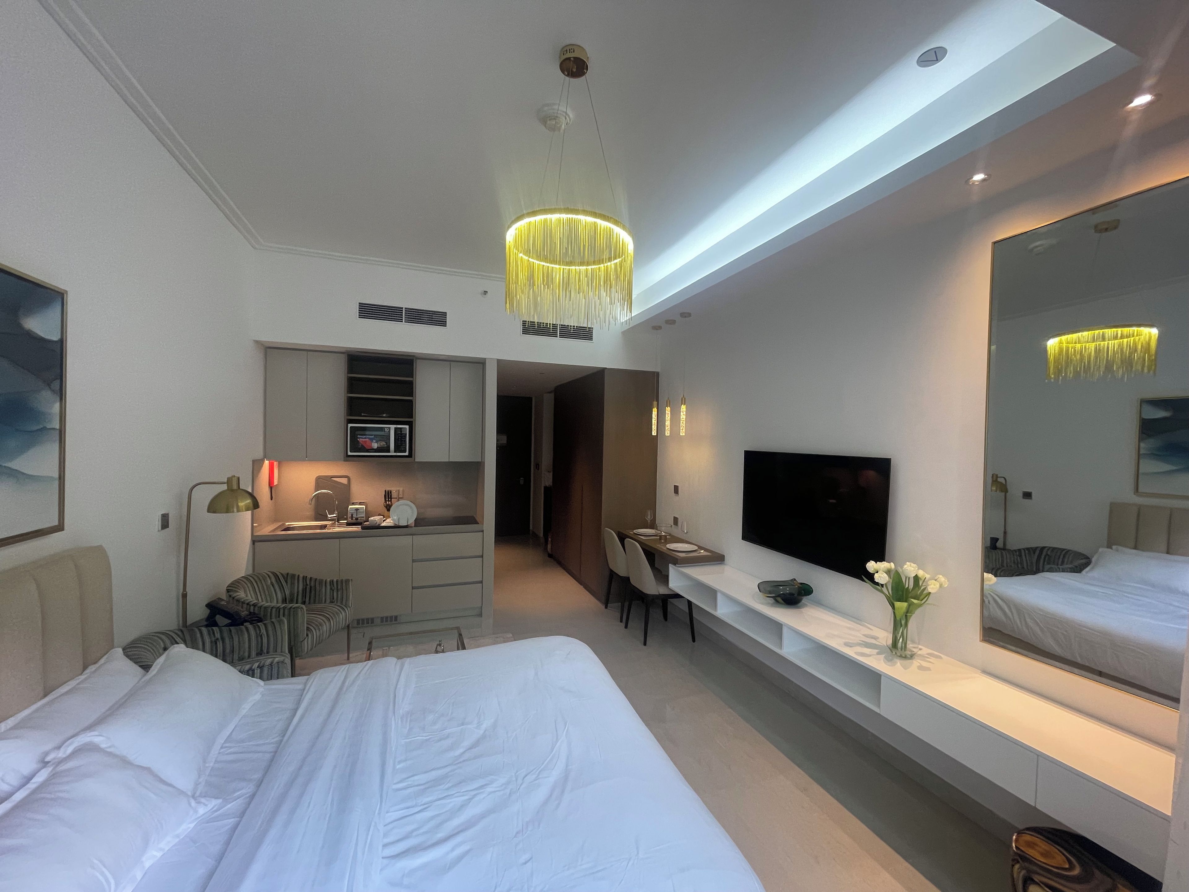 Ein modernes Hotelzimmer mit einem großen Bett, einem Schreibtisch mit Fernseher, einer Küchenzeile und einem Badezimmer.