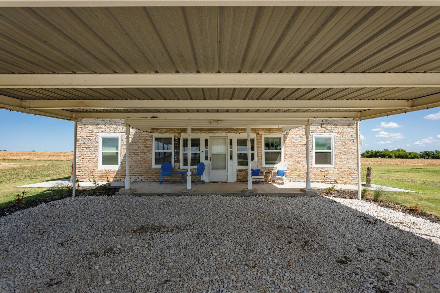 Un patio couvert avec un bâtiment en pierre, des sièges extérieurs et un sol en gravier.